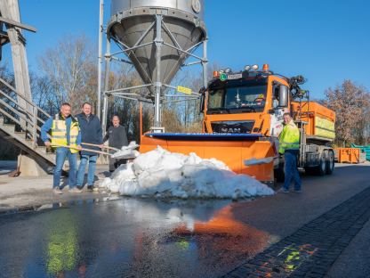 Mehrere Männer stehen mit einer Schneeschaufel in der Hand bei einem Haufen Schnee, im Hintergrund befindet sich ein Schneepflug