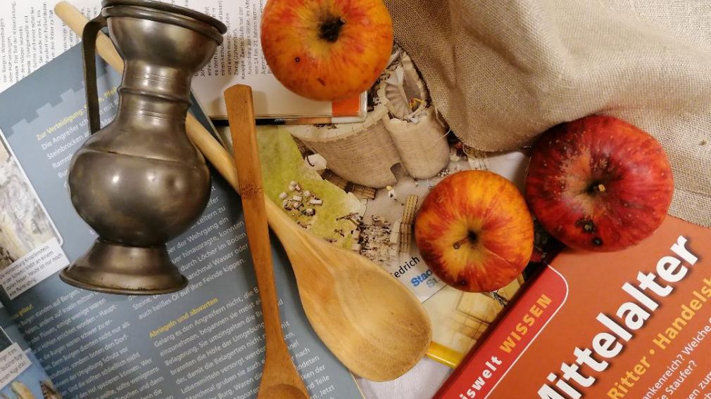 Äpfel, Kochlöffel und ein Buch auf einem gedeckten Tisch. (Foto: Eva Birk)