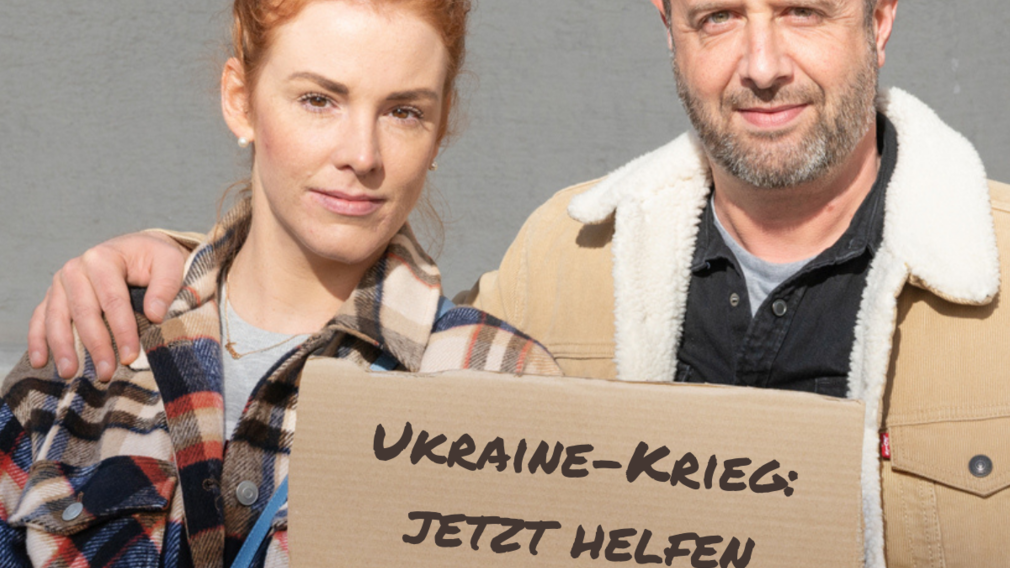 Eine Frau und ein Mann halten ein Schild mit der Aufschrift "Ukraine-Krieg: Jetzt helfen" hoch. (Foto: Caritas/Stefanie Steindl)