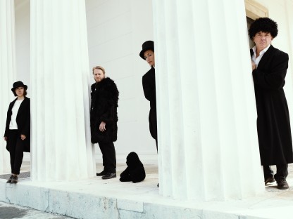 Schauspielerinnen und Schauspieler stehend bei weißen Säulen. (Foto: Alexi Pelekanos.)