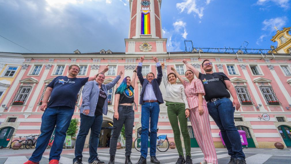 ST. Pride Vereinsmitglieder Erwin Rossmann, Elke Bandion, Tris Endl, Bürgermeister Matthias Stadler, Ilse Knell und Mariella Schlossnagl vom Büro für Diversität und ST. Pride Vereinsobmensch Oskar Beneder vor dem Rathaus mit Progress Pride Fahne am Rathausturm. (Foto: Arman Kalteis)