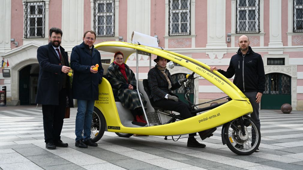 Eine gelbe Fahrrad-Rikscha mit Menschen die drinnen sitzen und rundherum stehen. (Foto: Arman Kalteis)