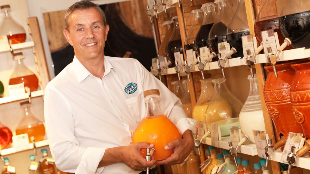 Gerhard Scholler steht zwischen den Regalen im Feinkost-Laden vomFASS St. Pölten und hält eine Flasche in der Hand. Foto: kommunikationsagentur-sengstschmid