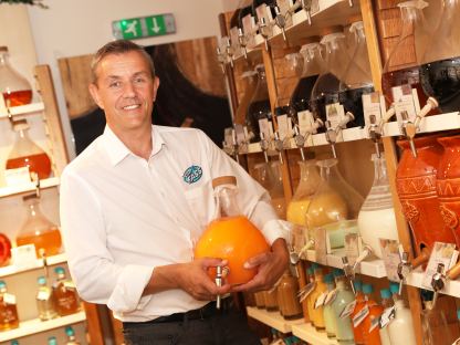 Gerhard Scholler steht zwischen den Regalen im Feinkost-Laden vomFASS St. Pölten und hält eine Flasche in der Hand. Foto: kommunikationsagentur-sengstschmid