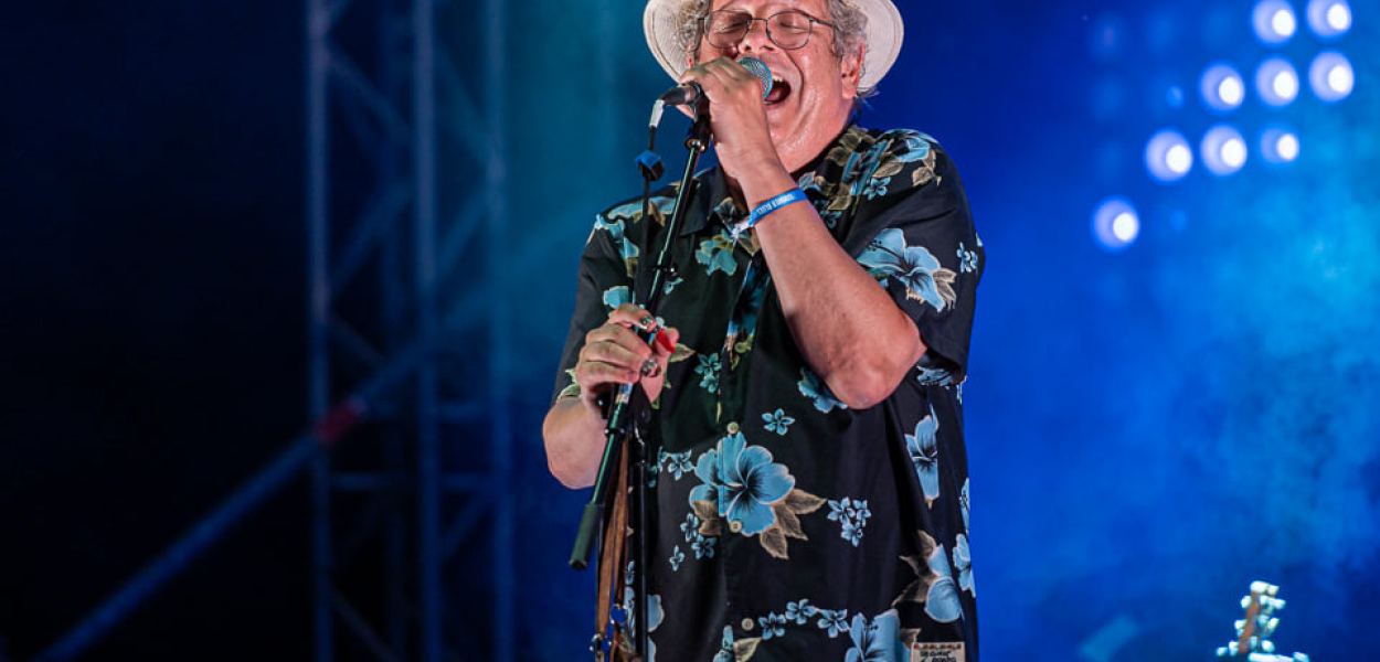 Ein Sänger einer Band mit einem Hut und einem Mikrofon auf der Bühne mit blauer Beleuchtung. (Foto: Christian Huber)