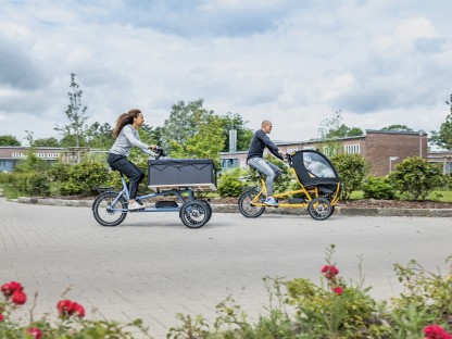 Vater, Mutter und Kind fahren mit einem Lastenrad durch die Stadt.
