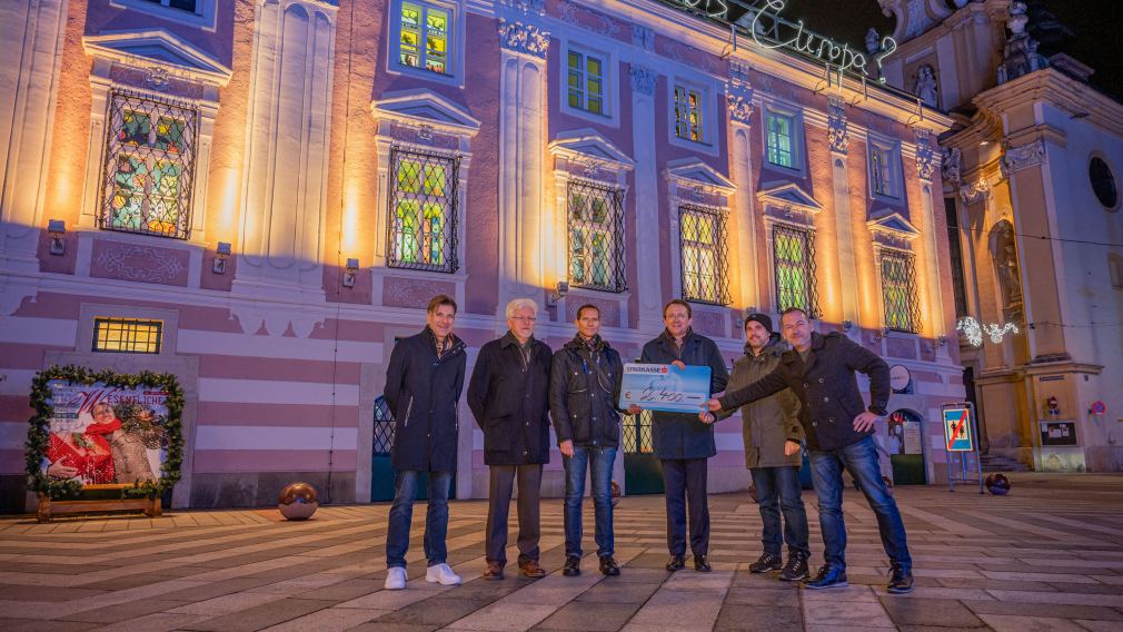 Sechs Personen mit Spendenscheck vor dem Rathaus mit beleuchteten Fenstern. (Foto: Kalteis)