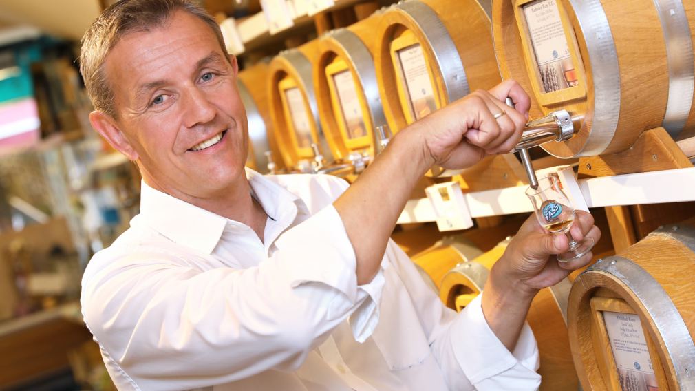 Gerhard Scholler steht zwischen den Regalen im Feinkost-Laden vomFASS St. Pölten und hält eine Flasche in der Hand. Foto: kommunikationsagentur-sengstschmid